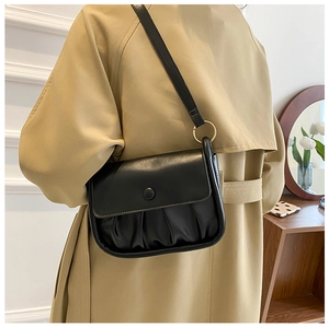 Detail of a black pleated cloud bag shown on a camel trench coat for a stylish look