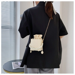 Detail of cream mini bucket bag featuring pearl handle and drawstring inner pouch