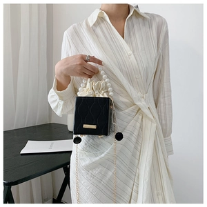 Detail of black leather bucket bag featuring white pearl handle and drawstring closure