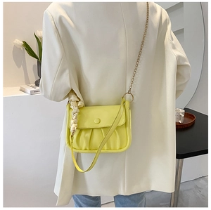 Detailed view of yellow ruched cloud bag with silk scarf and gold chain strap on a white suit