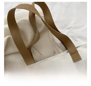 Close-up of wide brown woven strap and cross-stitch detail on white canvas tote bag