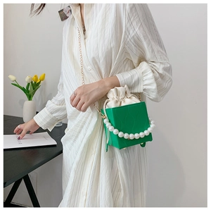 Detail of green bucket bag with pearl wrap and drawstring closure over striped shirt