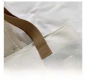 Close-up of white canvas tote bag showing brown woven handles and durable front zipper pocket