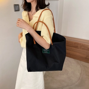 Borsa tote in tela nera minimalista con manici in pelle marrone e dettaglio etichetta verde
