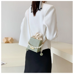 Detail of light green bucket bag with pearl handle and wave pattern on white blazer