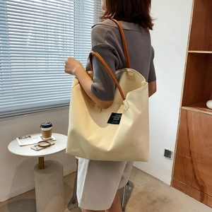 Minimalist canvas tote bag with brown leather straps and green patch for casual daily use