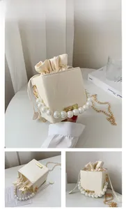 Detail of cream bucket bag with pearl handle, wavy texture and gold chain strap
