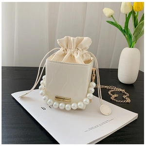 Detail of cream bucket bag featuring pearl handle and textured faux leather finish
