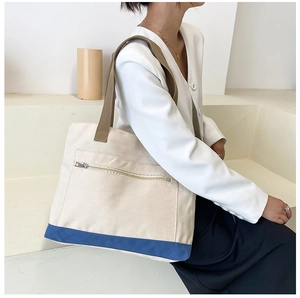 Detail of canvas tote bag with contrast navy trim and front zipper pocket on model