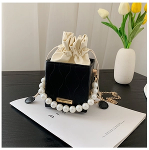 Detail of elegant black bucket bag with pearl handle and golden chain on a magazine