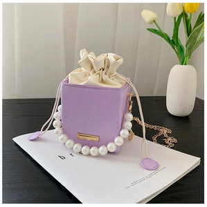 Detail of light purple bucket bag with wave texture, pearl handle and gold chain strap