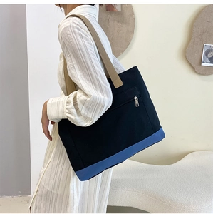 Side view of a large black canvas tote bag with blue base panel and khaki strap worn by a model