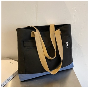 Detail of black canvas tote with khaki handles and front zipper pocket on metal table