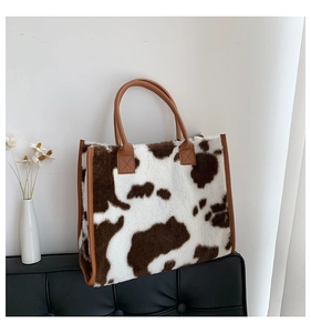 Dettaglio della borsa tote soffice con stampa mucca e manici in pelle marrone su panca