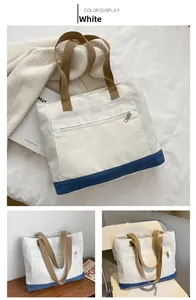 Detail of white canvas tote bag with dark blue base and beige straps shown on a desk