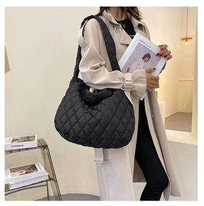 Borsa tote nera trapuntata con ampia tracolla indossata da una modella in un interno moderno