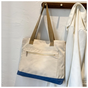 Detail of canvas tote bag showing blue base and front zipper pocket on wooden hook