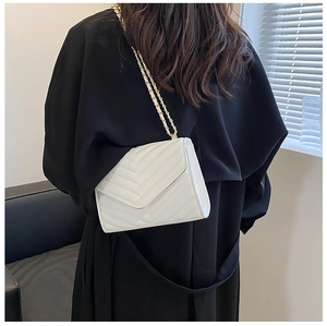 Vue de dos du sac enveloppe blanc matelassé en V avec chaîne dorée sur manteau noir