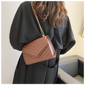 Détail du sac bandoulière marron matelassé en V avec chaîne dorée porté par un mannequin