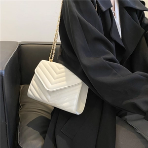 Sac à bandoulière blanc matelassé en V avec chaîne dorée porté par un mannequin chic