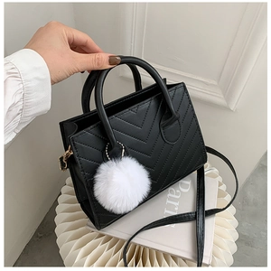 Detail of black V-quilted faux leather crossbody bag with white pompom on Paris prop book