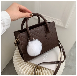 Close-up of chocolate brown tote with V-quilted stitching and white plush pom-pom charm