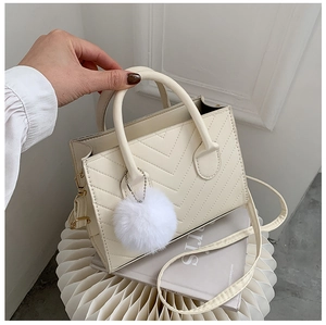 Detail of cream crossbody bag with V-shaped quilting, gold hardware, and plush pom-pom charm