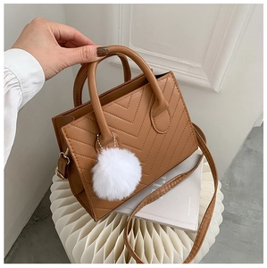 Detail view of brown chevron quilted PU leather crossbody bag with white fur pompom charm
