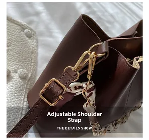 Détail de la bandoulière réglable en cuir avec boucle dorée sur un sac seau brun
