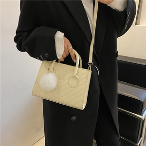 Chic cream quilted crossbody bag with top handles and faux fur pom-pom charm detail