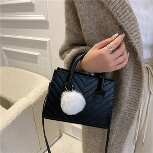 Chic black quilted crossbody handbag with a stylish white pompom charm on a model