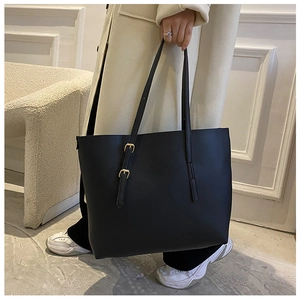 Close-up of black leather tote bag with gold buckle detail and beige coat lifestyle view