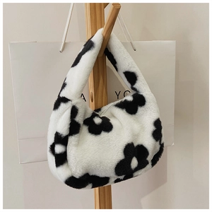 Detailed texture of white faux fur tote bag with black floral pattern on a wooden hanger