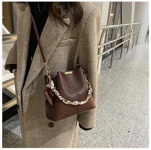 Détail du sac seau en cuir marron avec chaîne dorée et foulard en soie sur manteau beige
