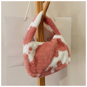 Close-up of pink and white cow print faux fur tote bag hanging on a wooden rack