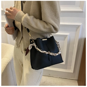 Détail d'un sac seau noir mat avec une chaîne enroulée d'un foulard en soie et logo doré