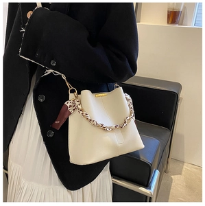 Détail d'un sac seau blanc avec chaîne dorée et foulard en soie porté par un mannequin