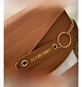 Detail der braunen Satteltasche mit Krokodilprägung, Goldkette und Stoffgurt