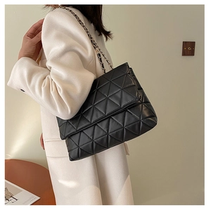 Sac à bandoulière noir matelassé avec chaîne dorée porté sur un tailleur blanc