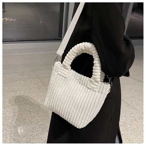 Detailed side view of white corduroy tote bag with pleated handle on a black coat