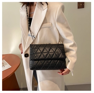 Détail d'un sac noir matelassé à chaîne porté avec un manteau beige élégant