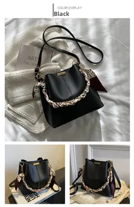 Détail du sac seau noir avec poignée en chaîne et foulard en soie sur une texture en cuir
