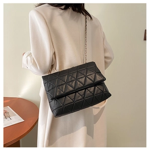 Détail d'un sac bandoulière noir matelassé avec chaîne porté par un mannequin