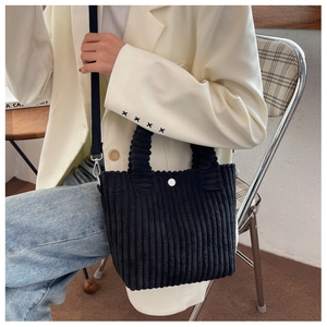Detail of black corduroy bucket bag with top handles and white button accent