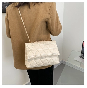 Détail d'un sac bandoulière beige matelassé avec chaîne dorée sur un bureau moderne