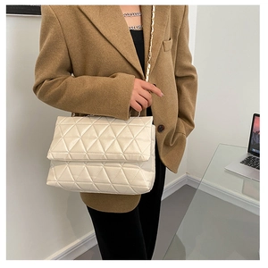 Détail d'un sac à rabat matelassé beige avec chaîne dorée sur un bureau professionnel