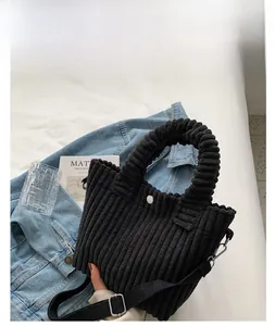 Detail of black corduroy bucket bag with wavy handle and fabric strap on white sheet
