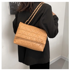 Petit sac bandoulière matelassé beige avec chaîne dorée porté sur un blazer noir