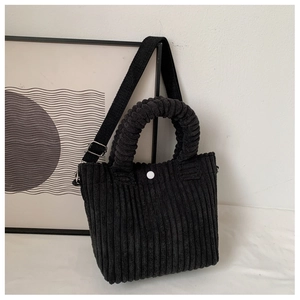 Detailed shot of black corduroy tote bag showing metal snap button and soft fabric texture