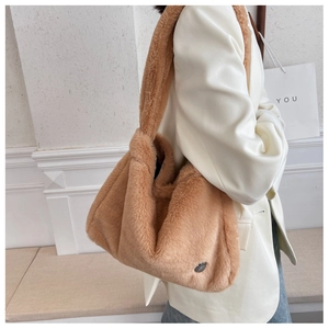 Close-up of caramel plush shoulder bag featuring soft faux fur texture and metal badge detail